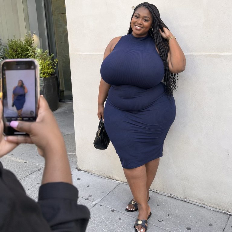 Femme posee devant un mur clair de la ville pendant que son amie la photographie en pied. Illustration de la photo pleine longueur sur un profil de rencontre